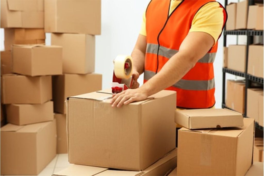 چند کارتتن مقوایی و یک فرد در حال بستّ بندی-بهترین روش بسته بندی کالا